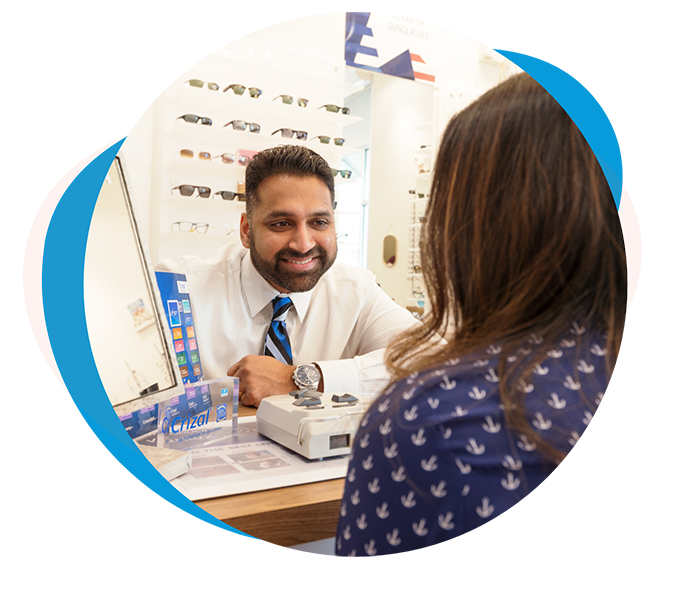 Woman trying on glasses at a desk in optometry office in Richmond