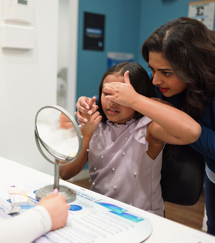 Optometrist helping a young girl patient put in a contact lens