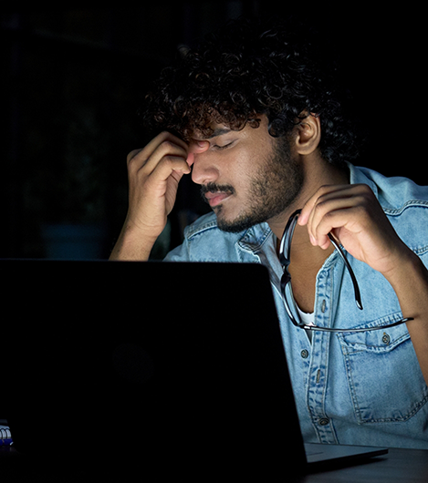 Man sitting in front of computer and pinching the bridge of his nose