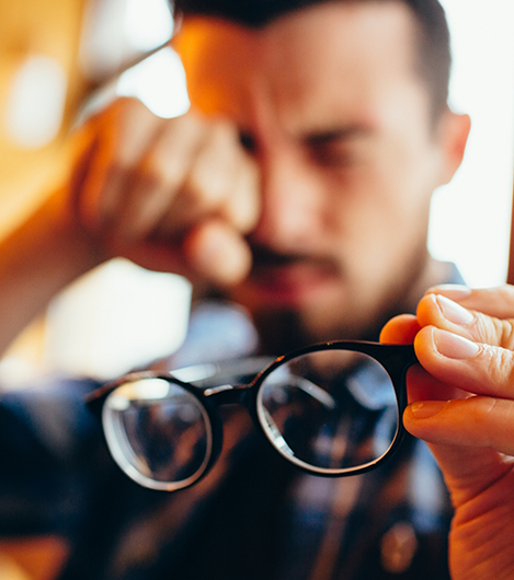 Blurry man rubbing his eyes while holding glasses