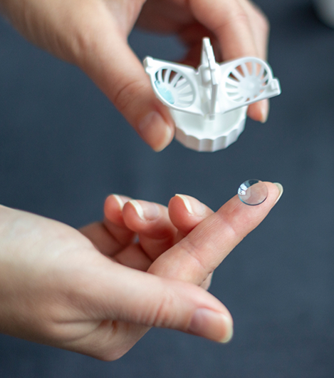 Person holding a contact lens in one finger and the case in the other hand