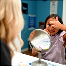 Young girl looking closely at her eye in a mirror